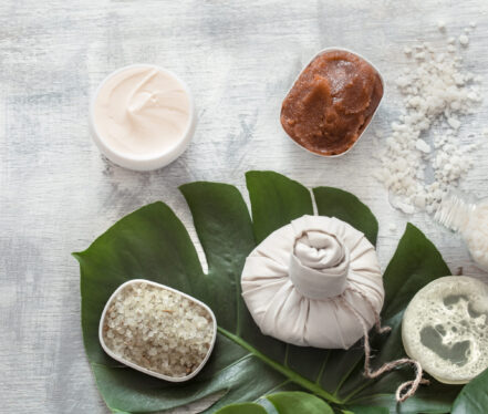 Flat-lay natural cosmetics and accessories with tropical leaves to cleanse the skin. Basic hygiene and body care items on white background, copy space.